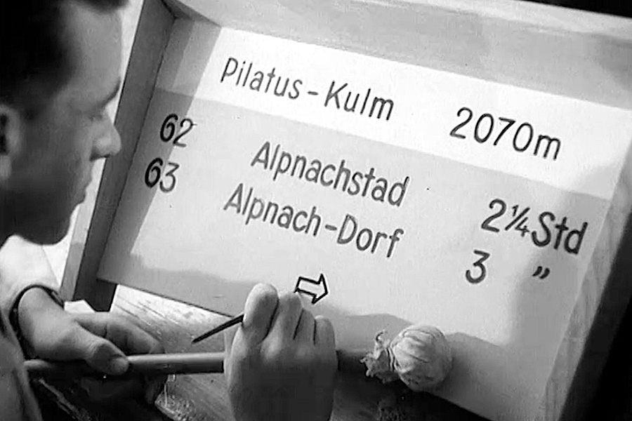 An der Luzerner Gewerbeschule stellen Schriftenzeichner Wegweiser für die Wanderwege am Pilatus her. Bild: Still aus der Schweizer Filmwochenschau «Freiwillige helfen mit bei der Markierung und Verbesserung der Pilatuswege»